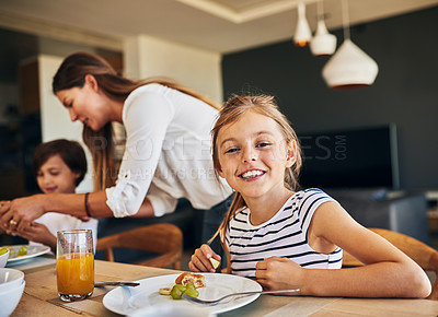 Buy stock photo Portrait of a little girl having breakfast with her family in the background