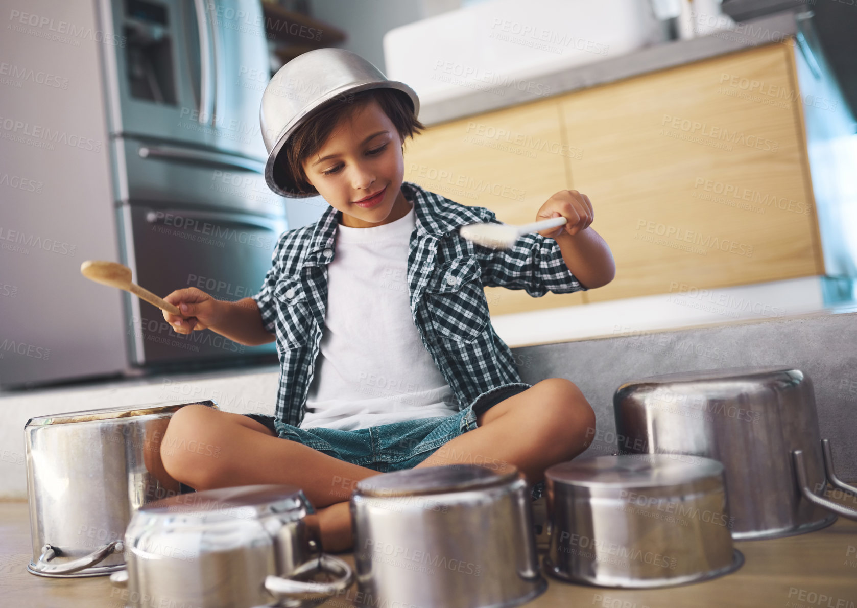 Buy stock photo Shot of a happy little boy playing drums with pots on the kitchen floor while wearing a bowl on his head