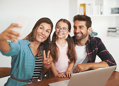 Buy stock photo Shot of a happy married couple and their young daughter posing for a selfie together at home