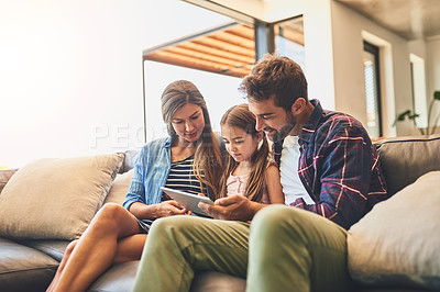 Buy stock photo Shot of a mother and father using a digital tablet with their daughter on the sofa at home