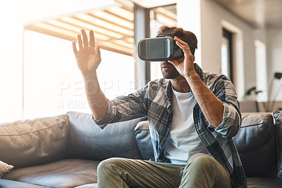 Buy stock photo Shot of a young man using a virtual reality headset on the sofa at home