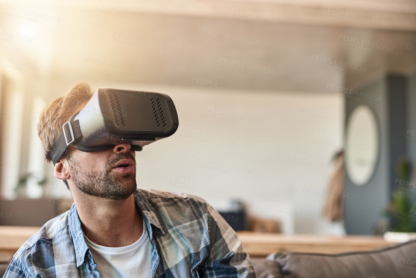 Buy stock photo Shot of a young man using a virtual reality headset on the sofa at home