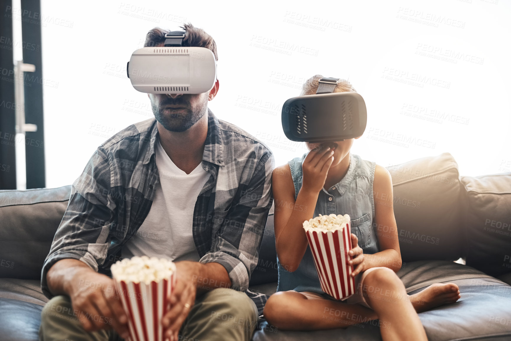 Buy stock photo Shot of a father and daughter eating popcorn and watching movies with virtual reality headsets at home