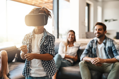 Buy stock photo Shot of a little boy using a virtual reality headset at home with his parents in the background