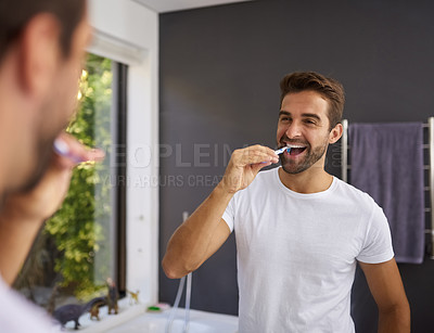 Buy stock photo Cropped shot of a handsome man looking in the mirror and brushing his teeth in the bathroom at home
