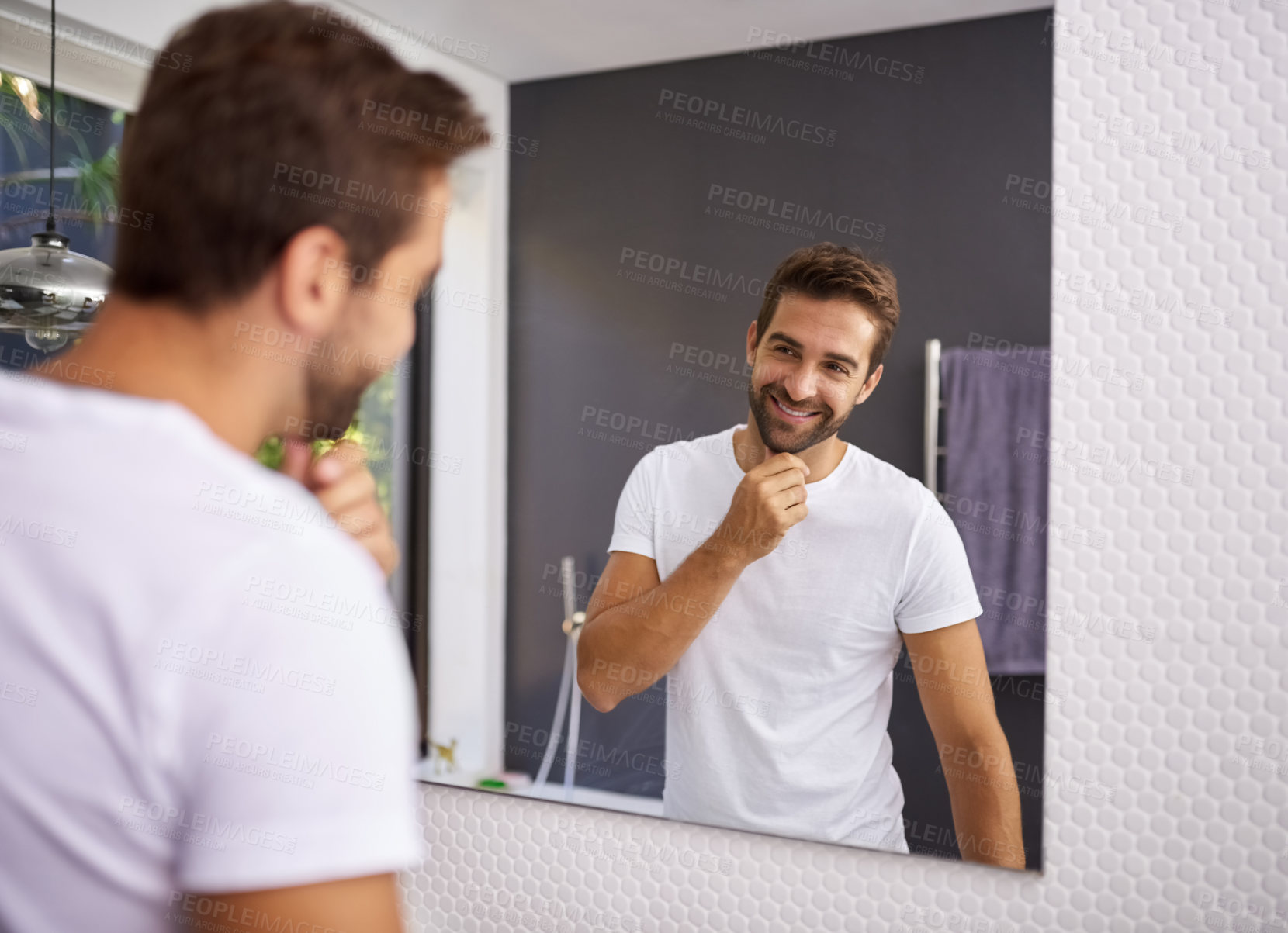 Buy stock photo Cropped shot of a handsome man looking at himself in the mirror whilst touching his beard at home