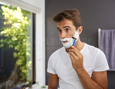 Buy stock photo Cropped shot of a handsome man shaving his beard in the bathroom at home