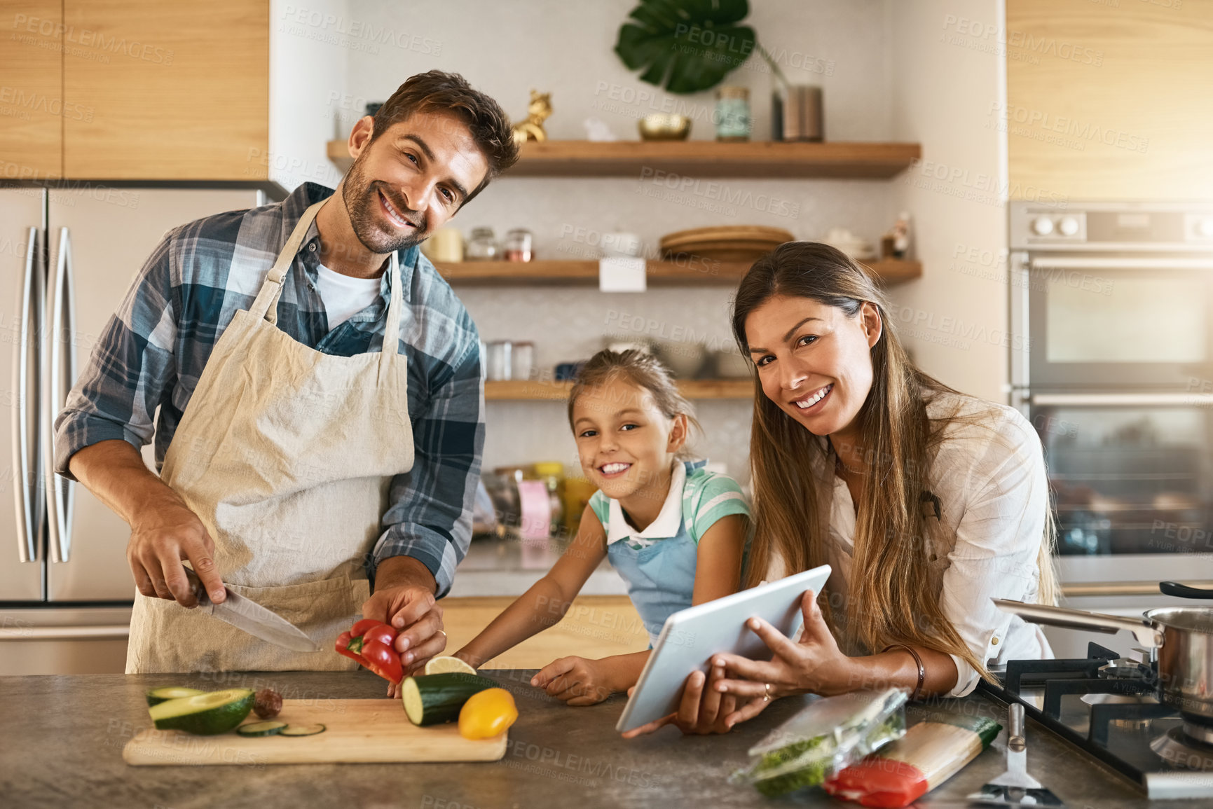 Buy stock photo Portrait of two happy parents and their young daughter trying a new recipe in the kitchen together