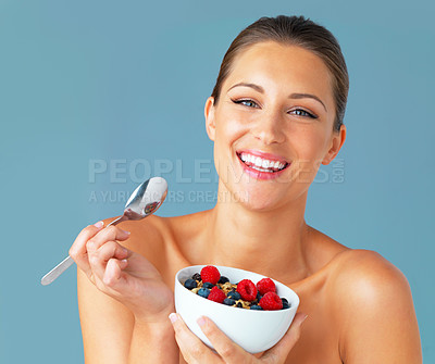 Buy stock photo Studio shot of an attractive young woman eating a bowl of muesli and fruit against a blue background
