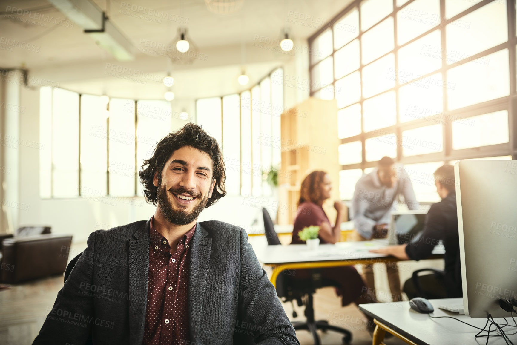 Buy stock photo Cropped portrait of a handsome young businessman sitting in the office with his colleagues in the background