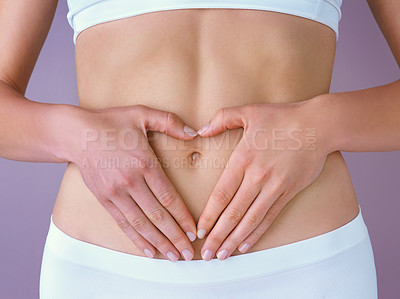 Buy stock photo Studio shot of a healthy woman using her hands as a heart shape frame on her stomach against a purple background