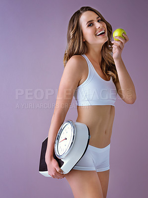 Buy stock photo Studio shot of a healthy young woman holding a scale and an apple against a purple background