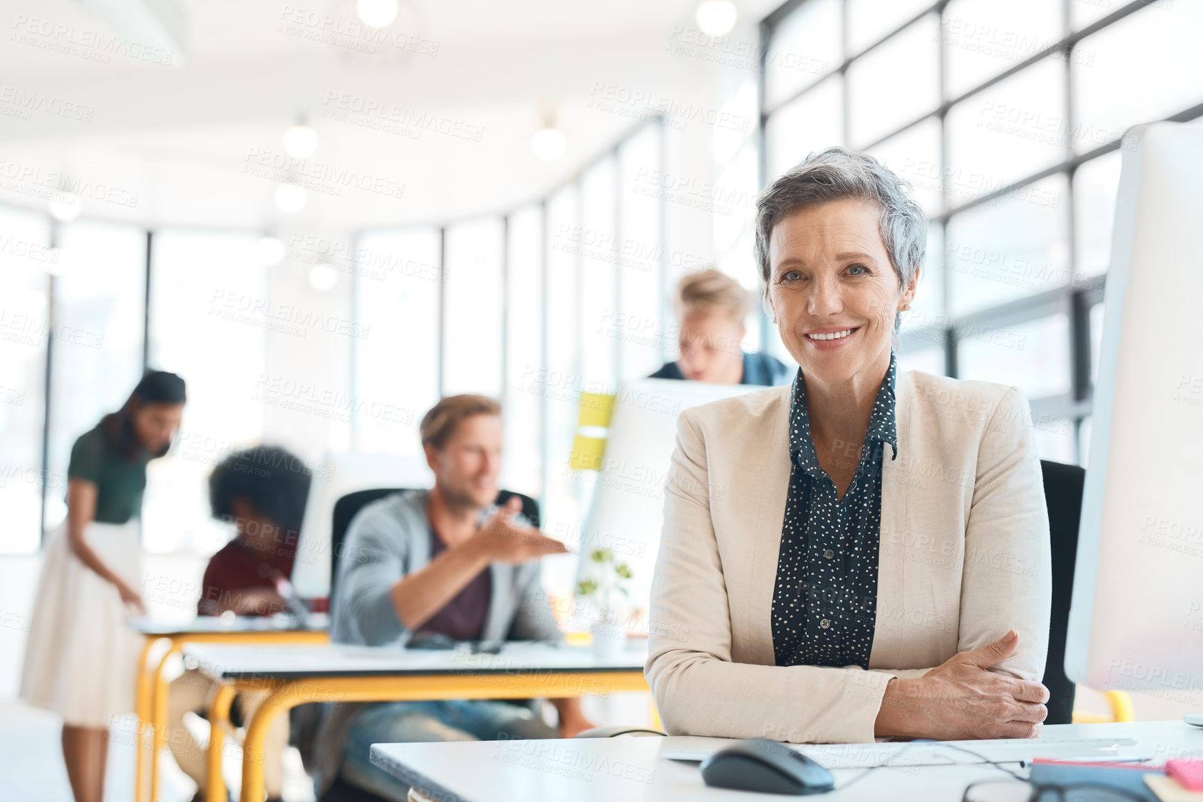 Buy stock photo Portrait of a happy designer sitting at her desk while her colleagues work in the background