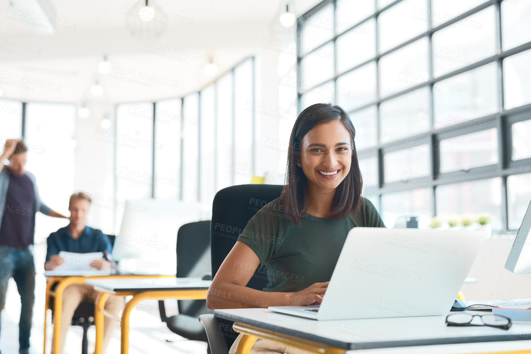 Buy stock photo Portrait of a happy designer sitting at her desk while her colleagues work in the background