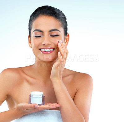 Buy stock photo Studio shot of a beautiful young woman applying moisturizer onto her face eyes closed against a blue background