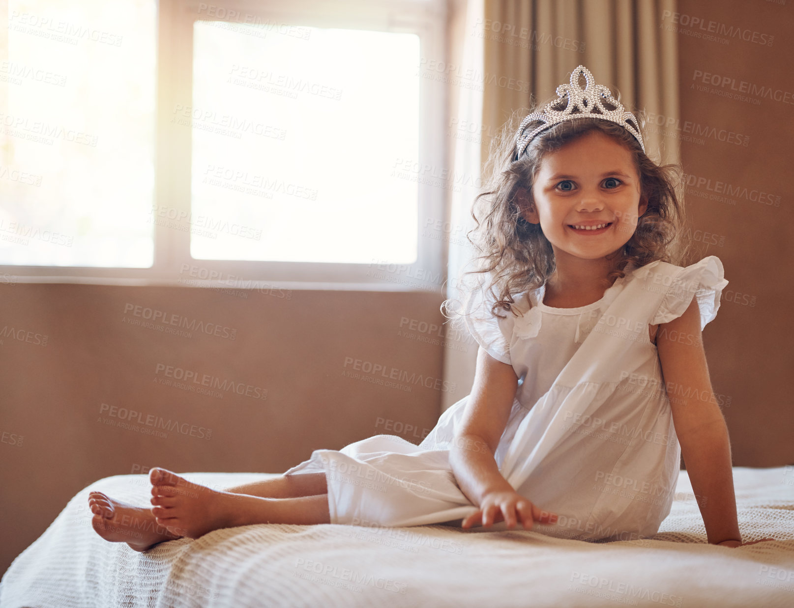 Buy stock photo Portrait of an adorable little girl wearing a tiara and sitting on a bed at home