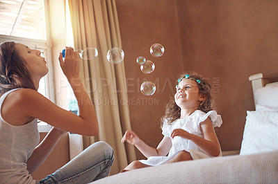 Buy stock photo Mother, girl and blowing bubbles in home for bonding, development and relationship together on bed. Woman, child and playing games in apartment with soap, water and toys for childhood fun activity