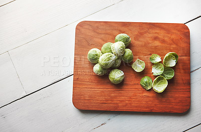 Buy stock photo Brussels sprouts, chopping board and cooking in kitchen for health, lunch and nutrition for wellness. Vegetables, food and wood block on table, above and meal prep for dinner on vegan diet in home