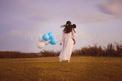 Buy stock photo Rearview shot of a young mother holding her son and balloons outdoors