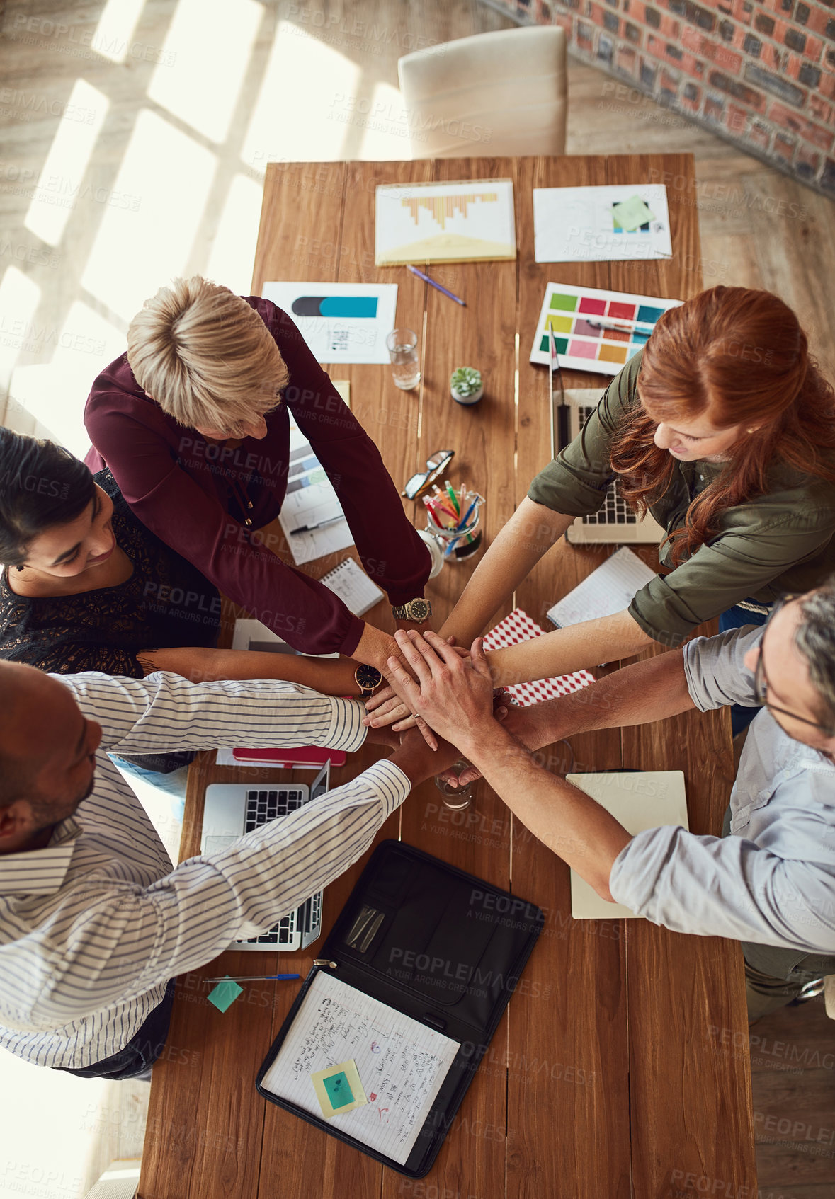 Buy stock photo High angle shot of a group of colleagues joining their hands in solidarity during a meeting in a modern office