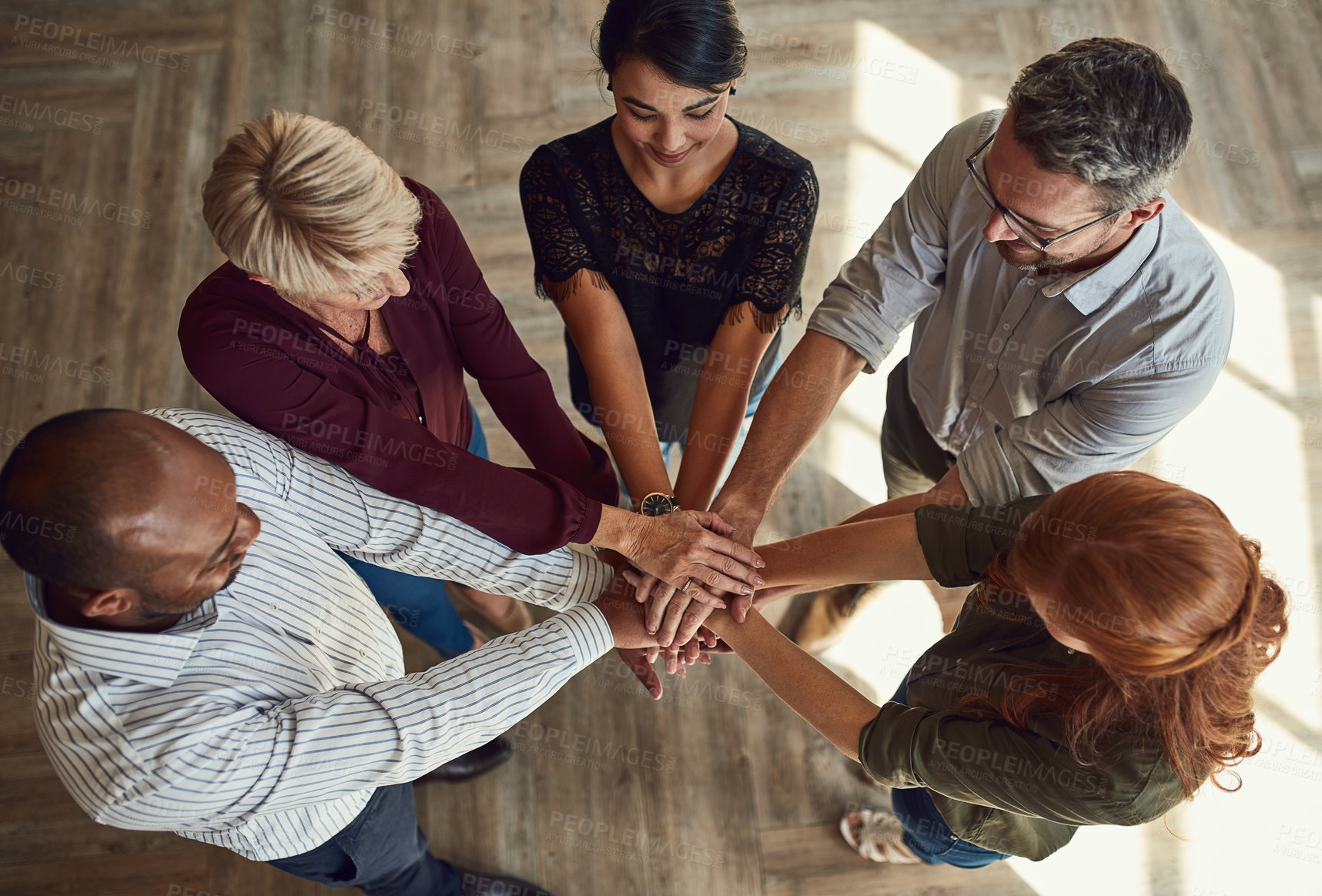 Buy stock photo A group of business professionals putting their hands together in unity, supporting each other and standing as a team top view. Diverse male and female design company employees uniting for a project