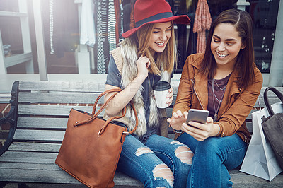 Buy stock photo Cropped shot of two young girlfriends sending text messages while sitting on a bench during a shopping spree