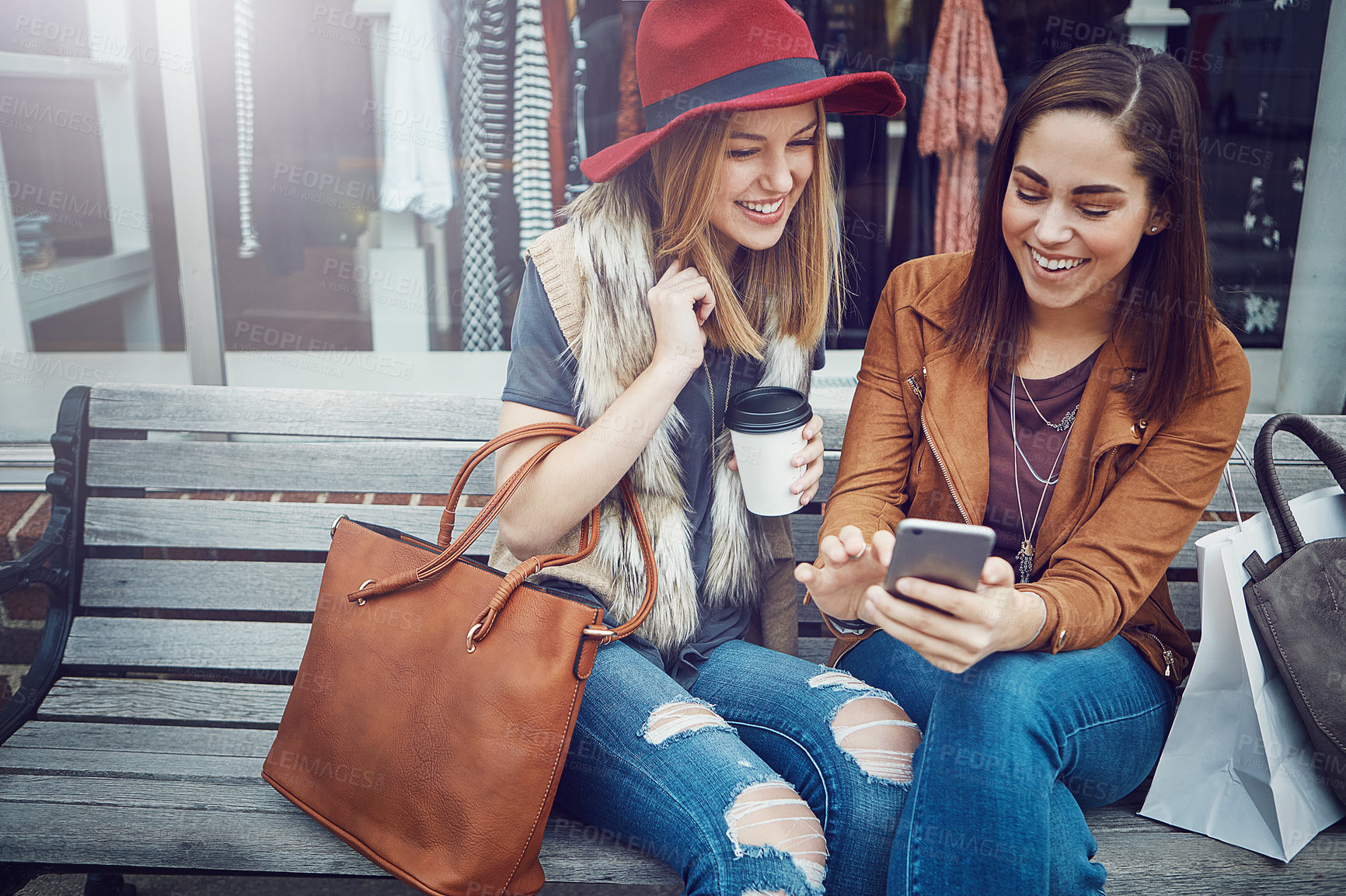 Buy stock photo Cropped shot of two young girlfriends sending text messages while sitting on a bench during a shopping spree