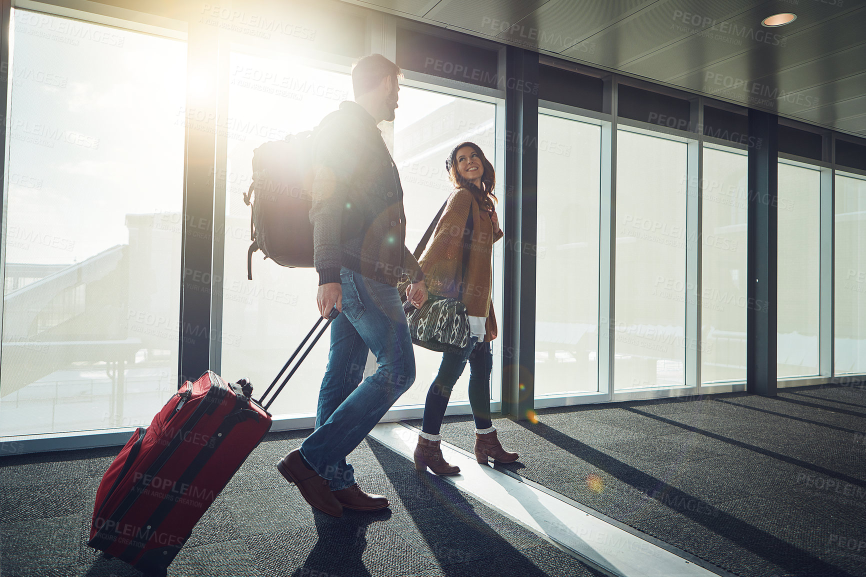 Buy stock photo Shot of a young couple walking together in an airport with their luggage while holding hands
