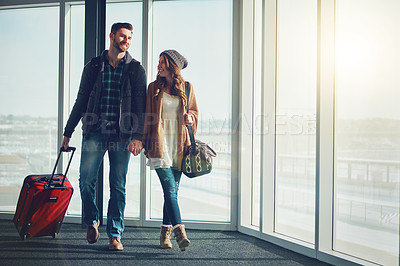 Buy stock photo Shot of a young couple walking inside of an airport with their luggage and holding hands