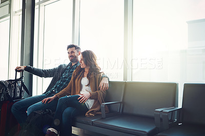 Buy stock photo Shot of a young couple sitting inside of an airport with their luggage holding one another