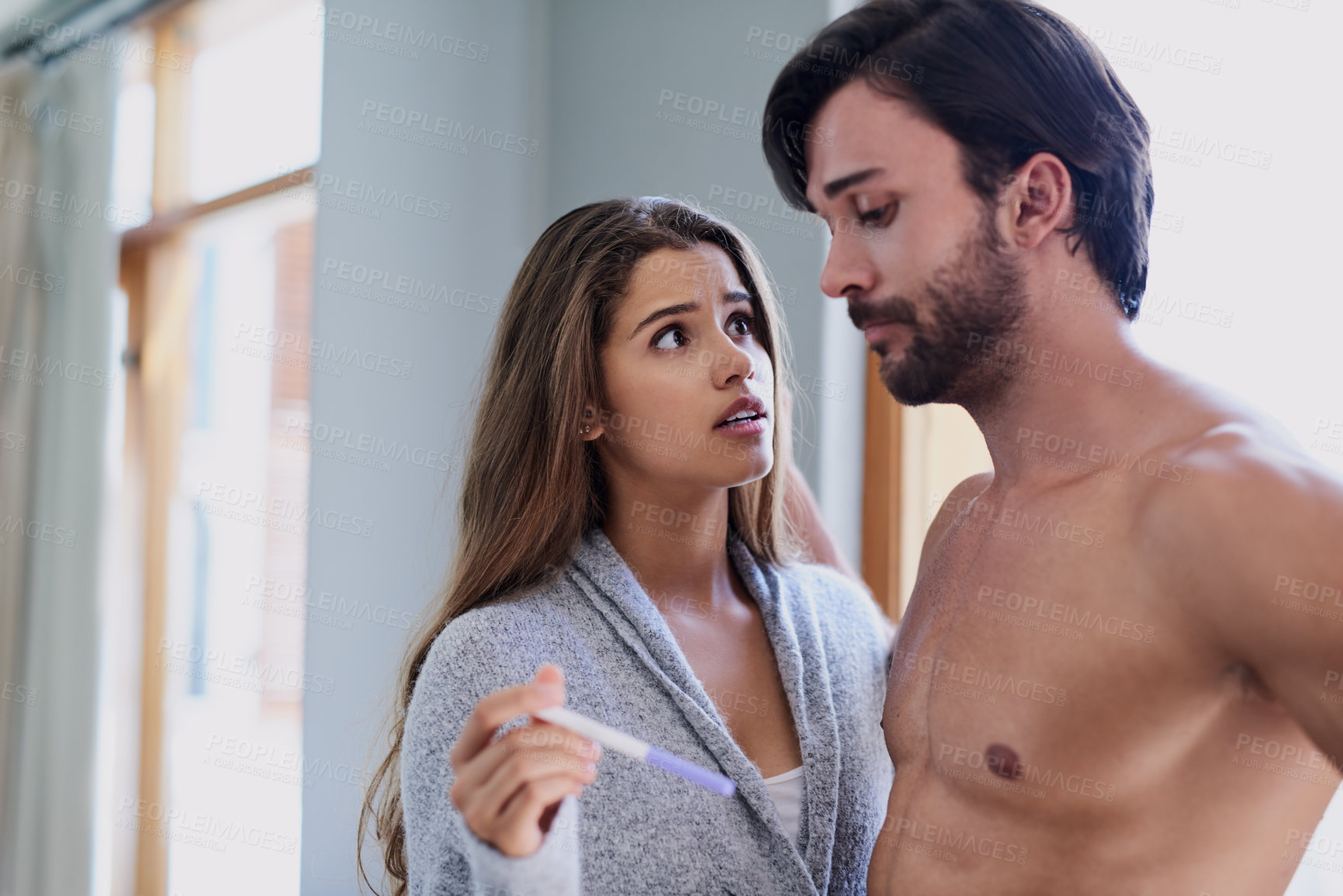 Buy stock photo Shot of a young couple looking worried while taking a pregnancy test at home