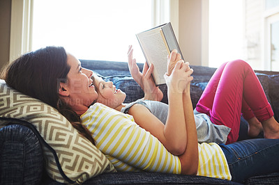 Buy stock photo Shot of a mother and her daughter reading a book together on the sofa at home
