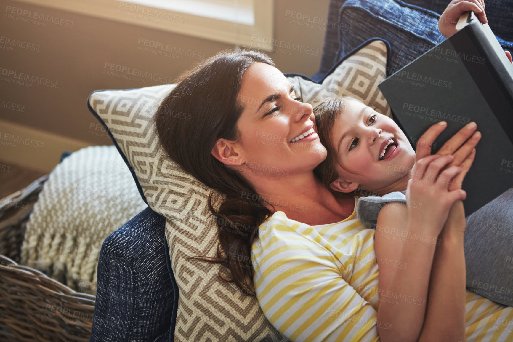 Buy stock photo Shot of a mother and her daughter reading a book together on the sofa at home