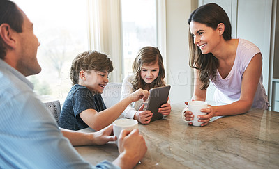 Buy stock photo Shot of a married couple and their young children playing with a tablet together in their kitchen