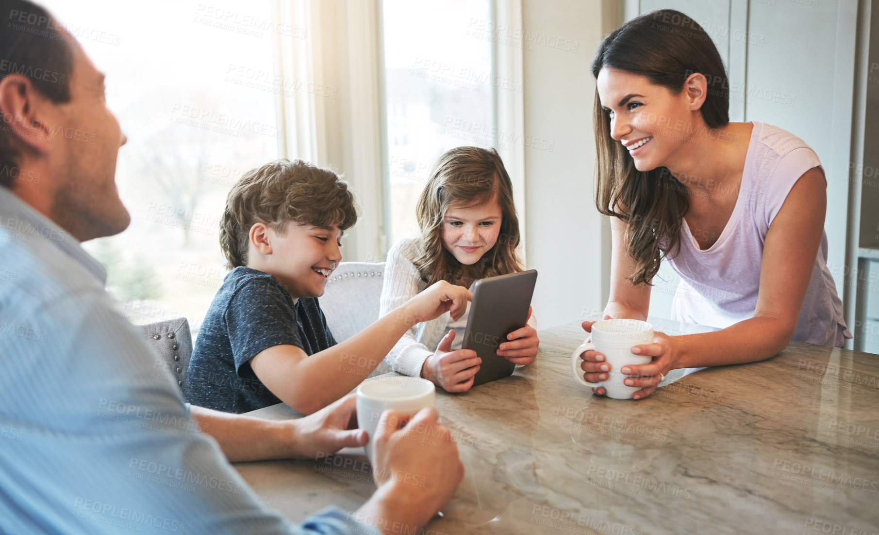 Buy stock photo Shot of a married couple and their young children playing with a tablet together in their kitchen