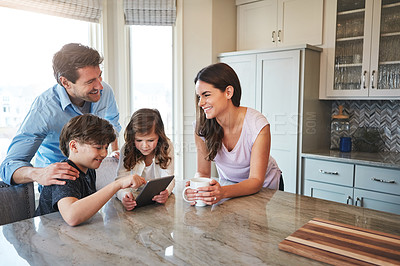 Buy stock photo Shot of a married couple and their young children playing with a tablet together in their kitchen