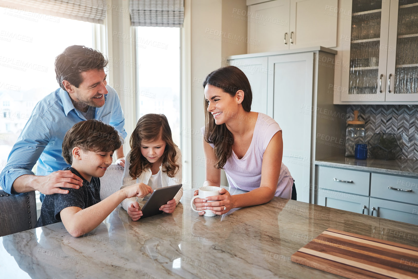 Buy stock photo Shot of a married couple and their young children playing with a tablet together in their kitchen