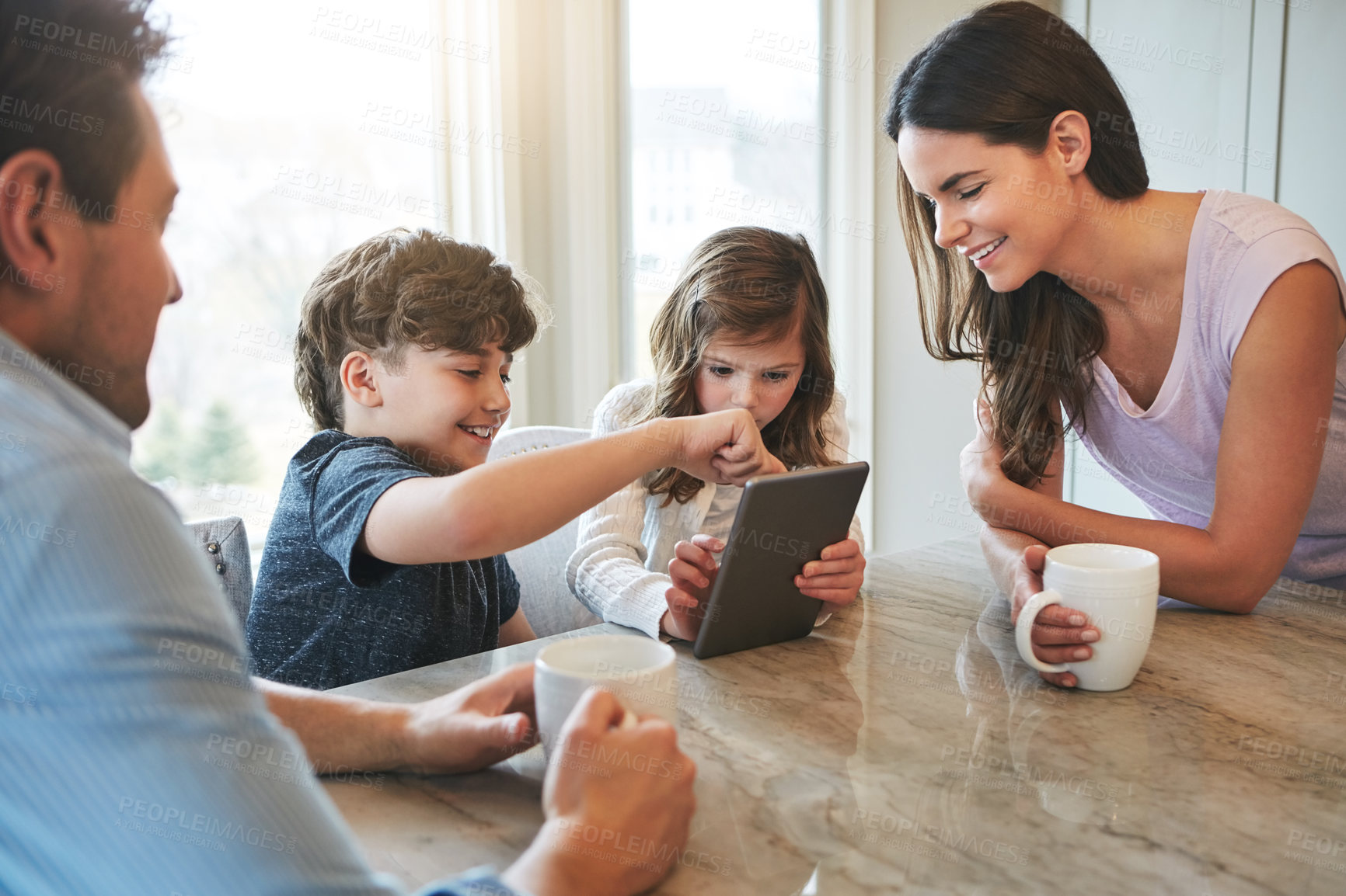 Buy stock photo Shot of a married couple and their young children playing with a tablet together in their kitchen