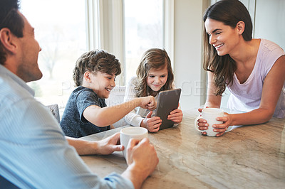 Buy stock photo Shot of a married couple and their young children playing with a tablet together in their kitchen