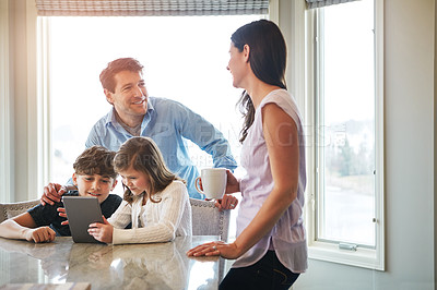 Buy stock photo Shot of a married couple and their young children playing with a tablet together in their kitchen