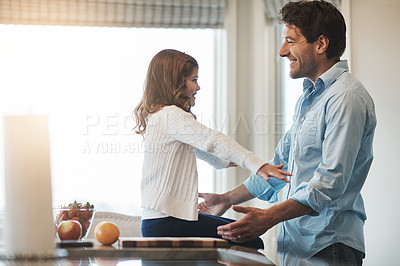 Buy stock photo Shot of a happy little girl reaching out to hug her father while sitting on the kitchen counter at home