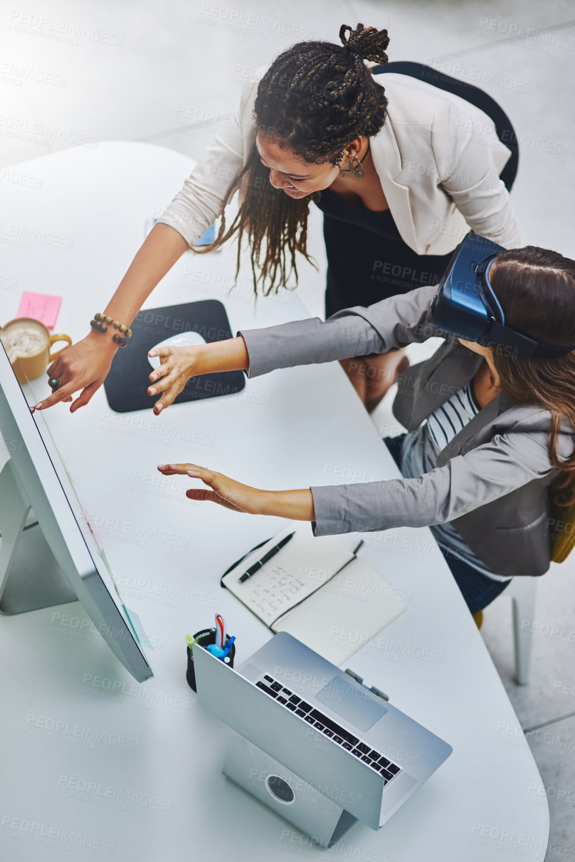 Buy stock photo High angle shot of a young businesswoman using a VR headset while being assisted by a female colleague