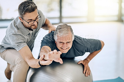 Buy stock photo Shot of a caring physiotherapist helping his mature patient to use a yoga ball at a rehabilitation center