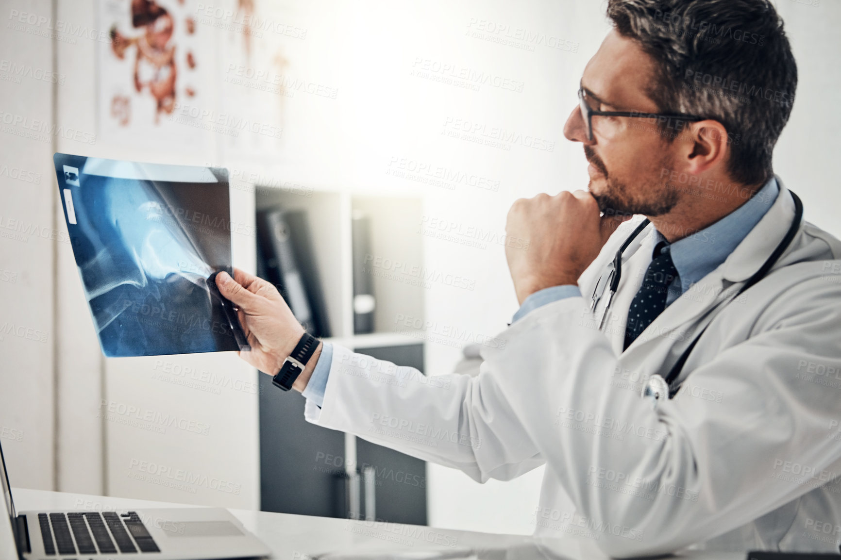 Buy stock photo Shot of a focused doctor looking at an x-ray while sitting at his desk