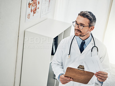Buy stock photo Shot of a focussed doctor reading a patient file while standing in his consultation room