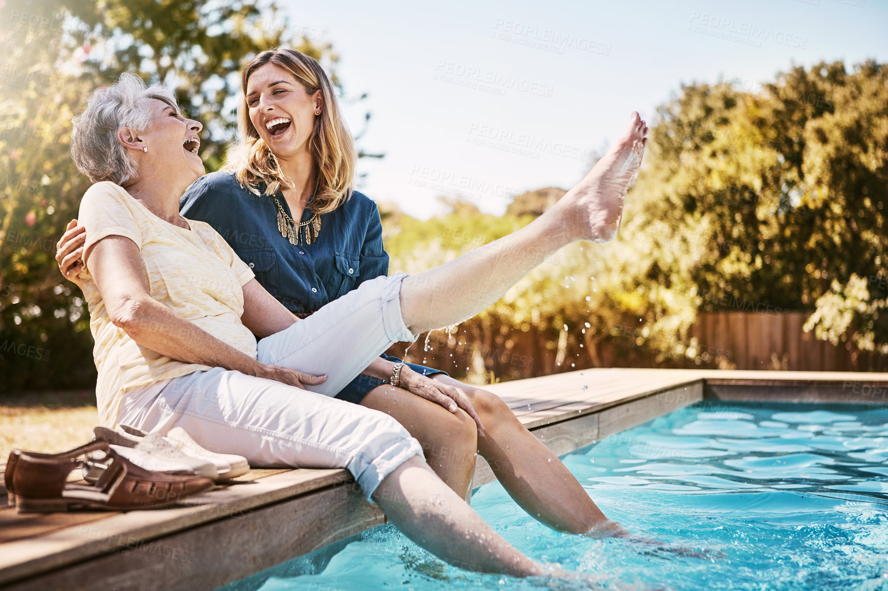 Buy stock photo Mother, daughter and happiness by swimming pool for wellness, hug or relax with lens flare in garden. Senior mom, woman and outdoor with smile for bonding, family with embrace or love and foot in air