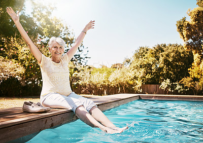 Buy stock photo Shot of a joyful senior woman dipping her feet in a swimming pool with her arms outstretched