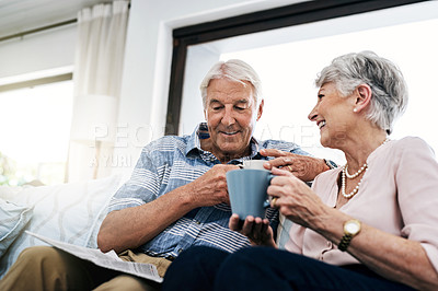 Buy stock photo Shot of a senior couple having coffee and reading a newspaper on the sofa at home