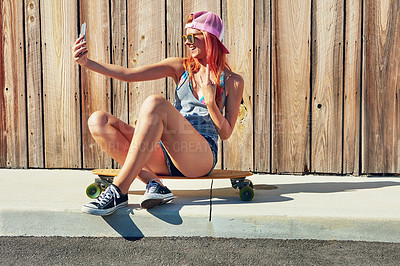 Buy stock photo Shot of a young woman taking a selfie while sitting on her skateboard