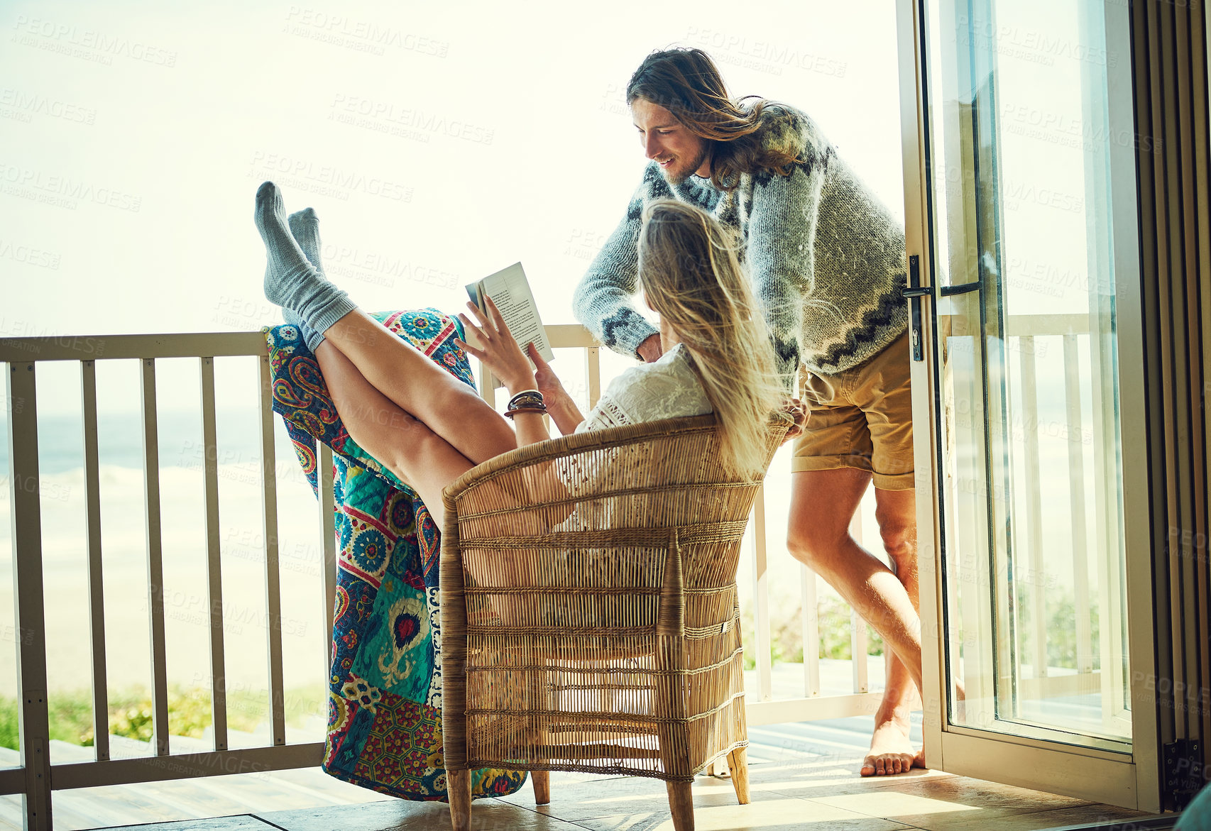 Buy stock photo Shot of a young couple reading a book together while relaxing on the balcony